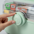 Hand closing a green container with a latch, showing a clear lid with labeled compartments.